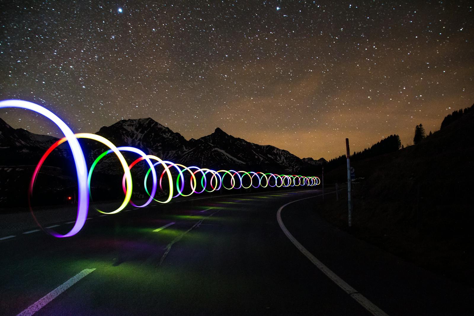 Enchanting long exposure of colorful light trails on a winding road beneath a star-filled sky.